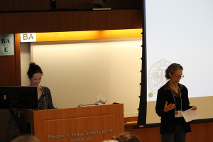 One woman stands in front of lecture hall introducing the guest speaker, who is standing behind a podium.